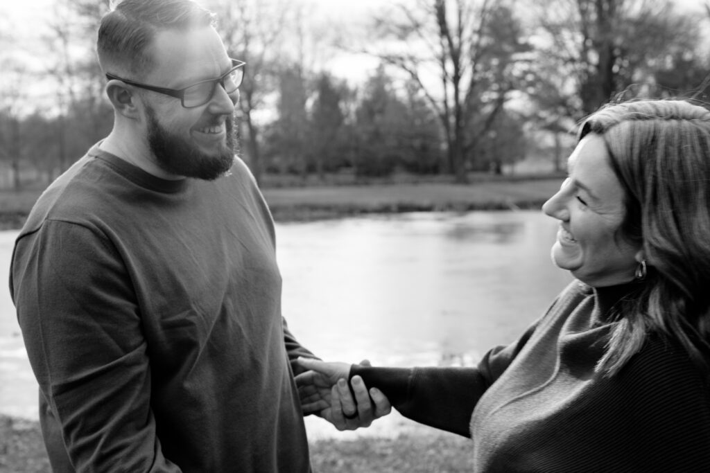 Black and white photo of a couple holding hands in front of a lake