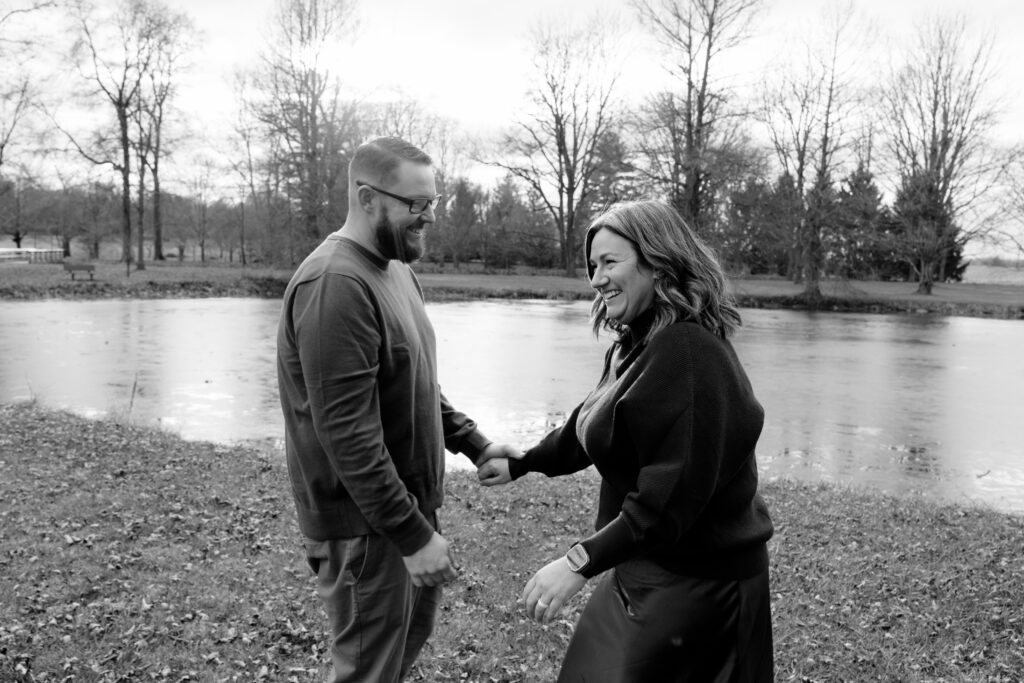 Black and white photo of a couple holding hands in front of a lake